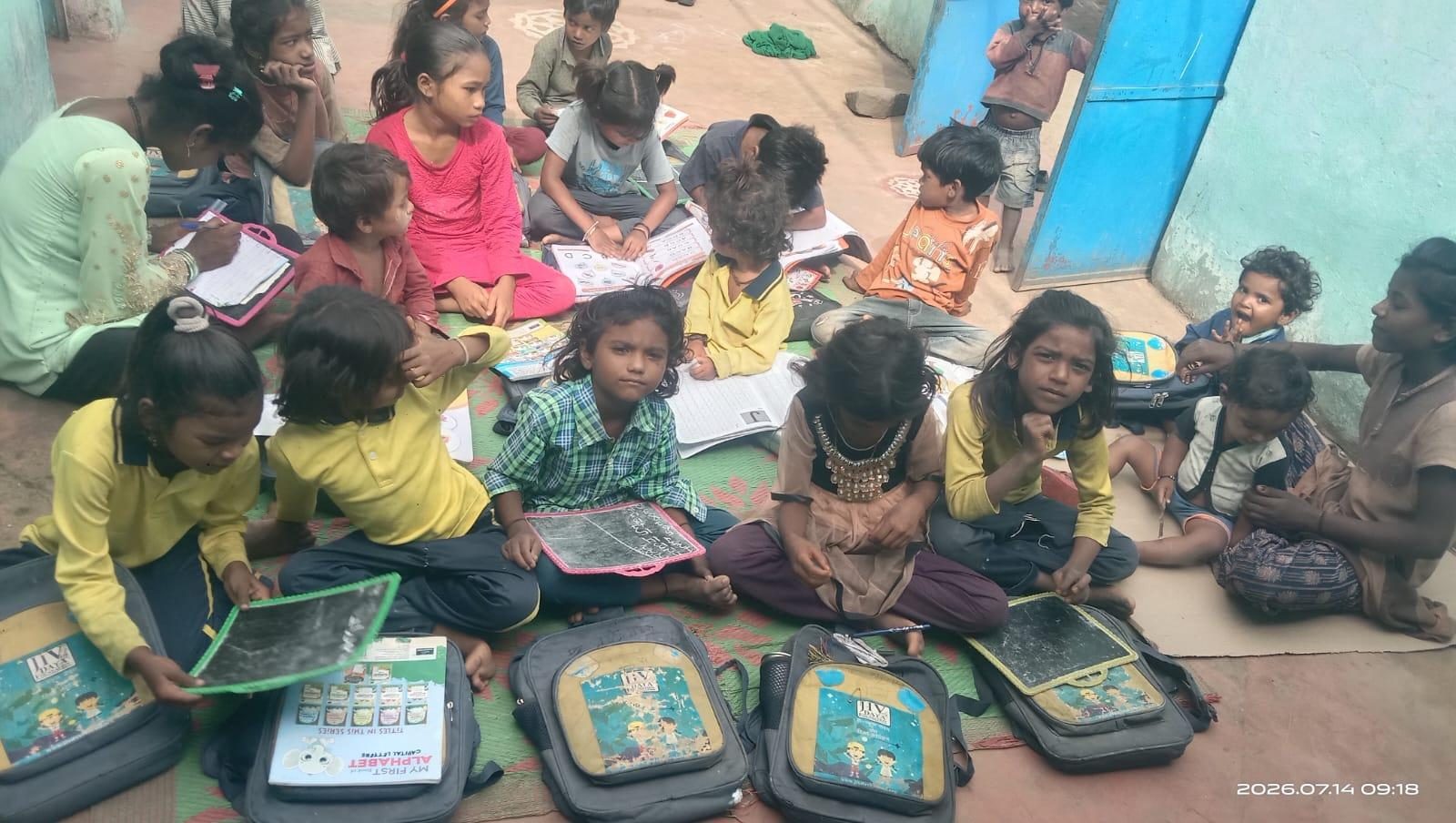 Children seated with school bags and learning material at a village centre