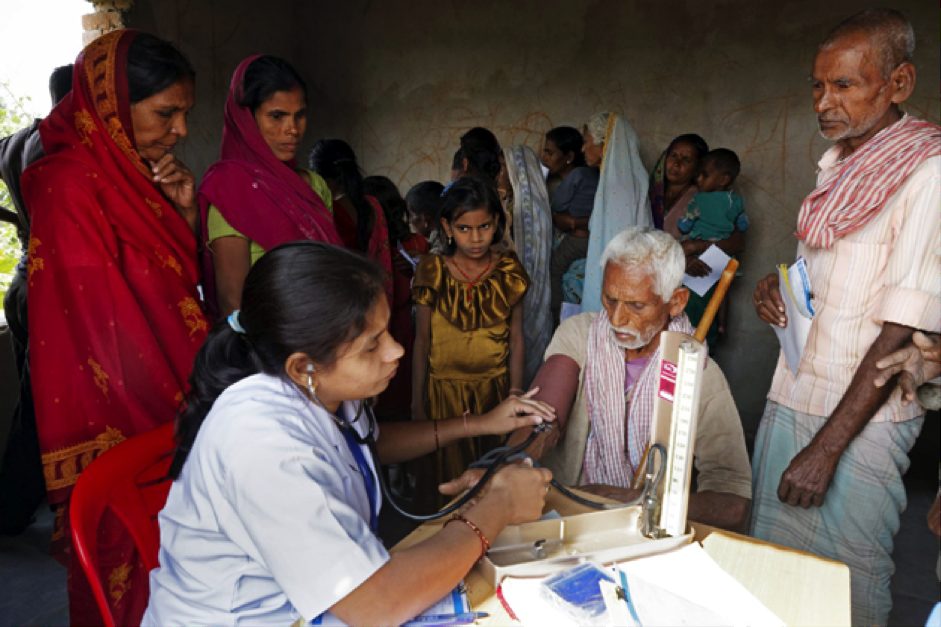 A health worker examines a patient while villagers wait their turn