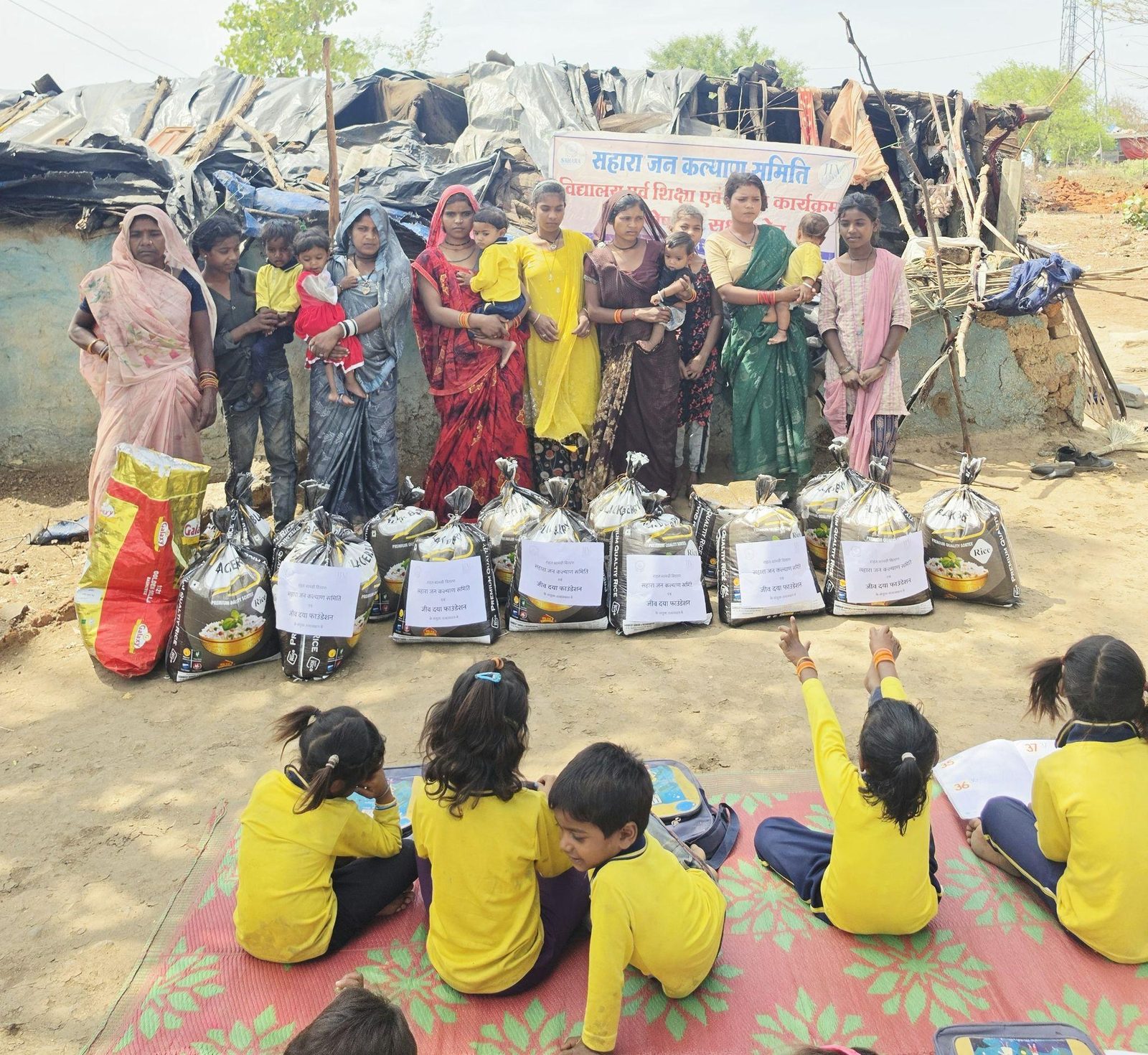 Ration kits laid out for distribution to families, with children seated in front