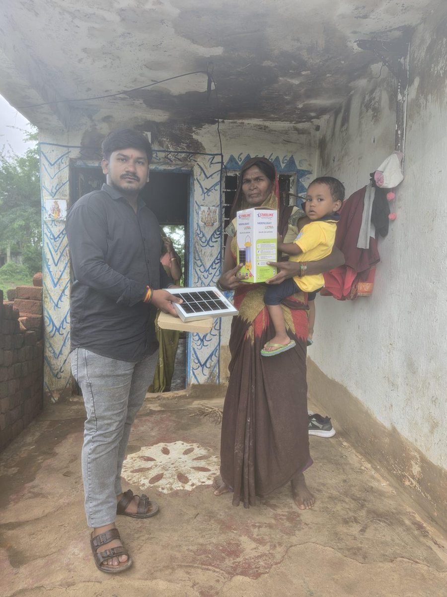 A mother, holding her young child, receiving her family's lantern: a household where nightfall previously meant complete darkness.